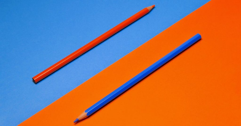 orange pencil on a blue background and blue pencil on an orange background facing opposite directions